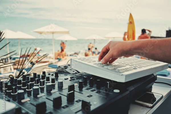 Fototapeta DJ hand and mixer close-up. Summer music party on the beach. On a blurred background people and the sea