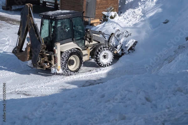 Fototapeta Tractor removing snow after snowfall. Winter season. Snow clearing. Tractor clears the way after heavy snowfall.