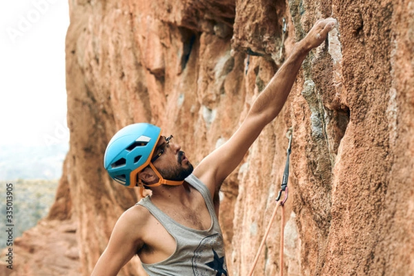 Fototapeta Escalador agarrando roca con una mano y mirando ruta