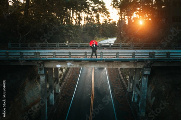 Fototapeta Person alone on bridge that is deserted over a deserted road with a red umbrella