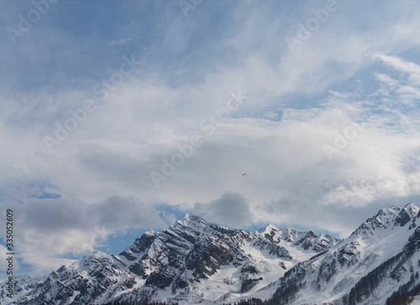 Fototapeta Peaks of snow-capped mountains against the blue sky with clouds