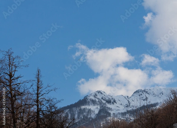 Fototapeta Peaks of snow-capped mountains against the blue sky with clouds