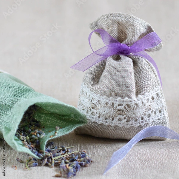 Fototapeta Small linen sack filled with dried lavender decorated with lacework and violet ribbon coqueand and one sachet is opened. Top view on thenatural flaxen background. Square with copy space. Closeup