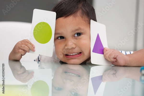 Obraz Young boy holding flash cards to learn about basic shape recognition and colors.