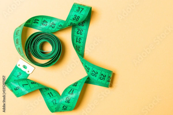 Fototapeta Top view of measure tape curtailed into a spiral with copy space. Concept of sewing accessory or healthy diet on orange background
