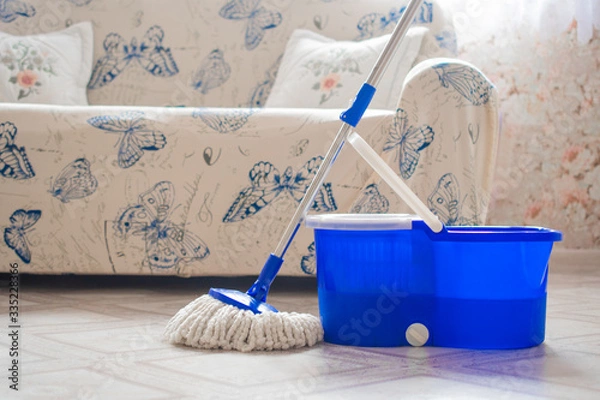 Fototapeta Round MOP and blue bucket on the light linoleum of the house against the background of a soft sofa: cleaning the house, disinfection from bacteria, germs, virus and dirt