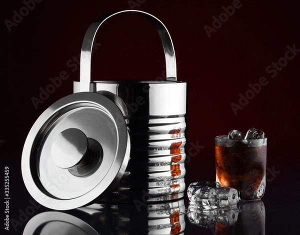 Fototapeta Pojemnik na lód. Szklanka z napojem i lodem. Lód ułożony na stole z odbiciem w szkle.