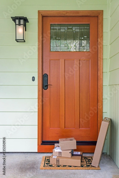 Obraz Recently delivered packages sit on a welcome mat in front of a wooden door to a residence.