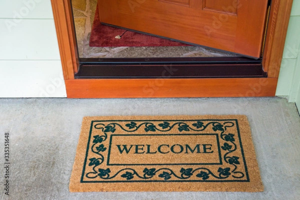 Obraz Recently delivered packages sit on a welcome mat in front of a wooden door to a residence.