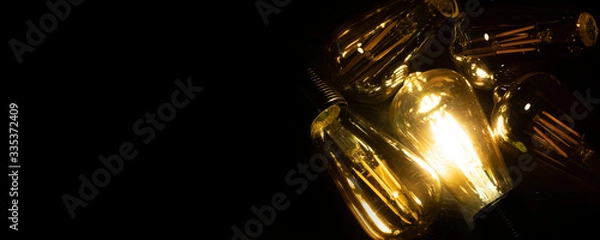 Fototapeta Invention, ideas and leadership concept; Close up glowing lighting bulb on dark black background. Panoramic aspect ratio for copy space. 