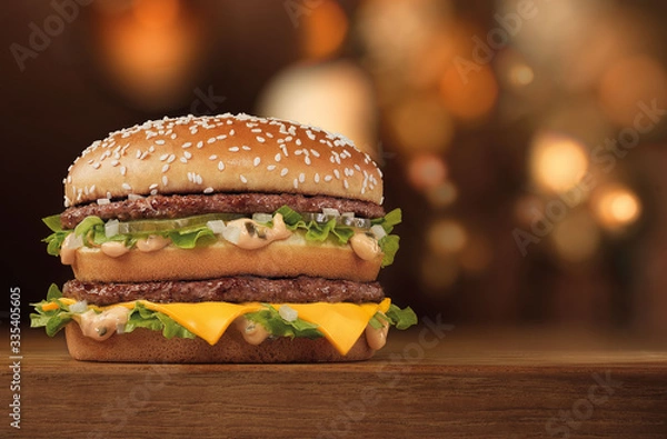 Fototapeta slender tall double burger with meat and cheese on a wooden table with bokeh on the background