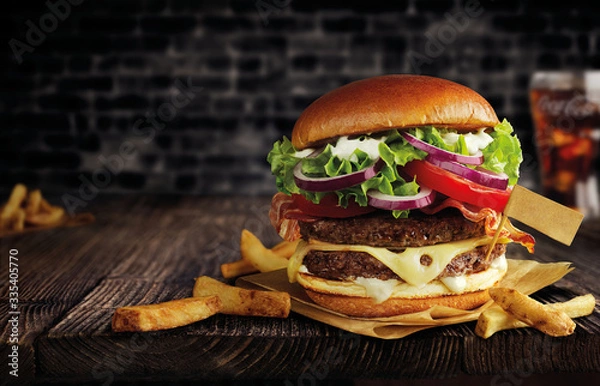 Fototapeta burger with double meat, cheese and french fries on a wooden table, with a flag, black brick wall behind