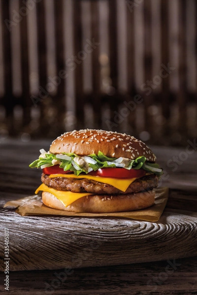 Fototapeta burger bun with sesame seeds, meat, cheese and on a wooden table and parchment, ready poster for printing