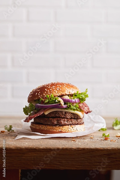 Fototapeta burger with sesame bun with onion rings and juicy fried meat on a white brick wall background, ready poster for print
