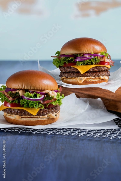 Fototapeta two burgers on a poster. with pork and cheese, with double meat and camembert with bacon on a metal grill and parchment