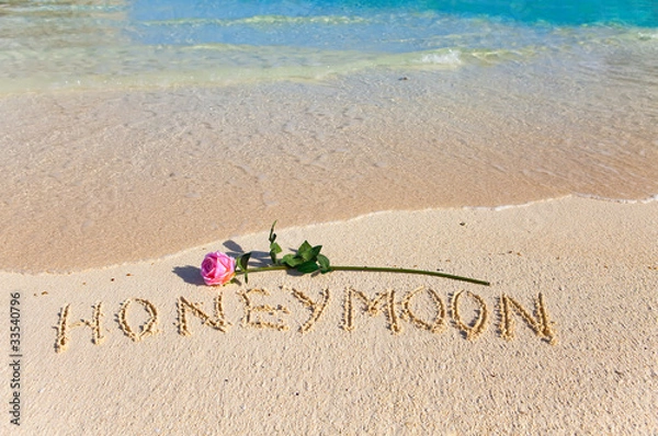 Fototapeta Na piasku napis „Honeymoon” i kwitnąca róża.