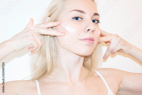 Obraz Beautiful blonde woman touching her perfect soft face skin with fingers, using face cream, cosmetology procedures.Spa, skincare and wellness. Close up, background, copyspace.