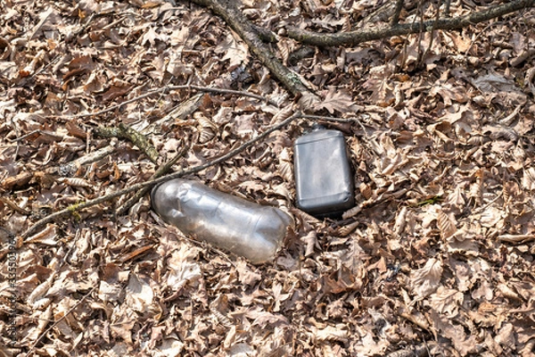 Fototapeta A dirty plastic and glass bottle left in the autumn forest. Plastic waste in the environment.