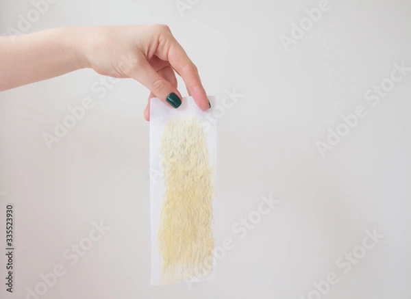 Fototapeta  used wax strips on a white background shows a young woman with a beautiful manicure