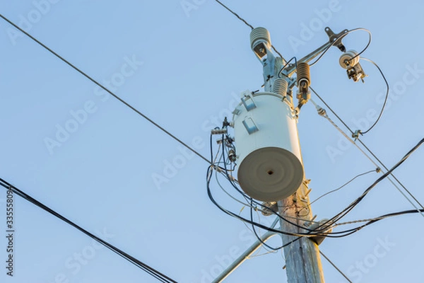 Fototapeta Power pole with transformer and power lines. Blue sky in the background. 