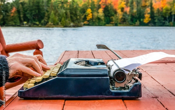 Fototapeta Work from anywhere - working on typewriter beneath the autumn sky while on a deck near the water's edge. concept - background