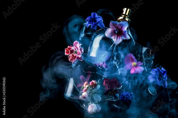 Obraz A glass perfume bottle shatters and bright spring flowers and clouds of blue and purple vapor burst out of it against a dark background