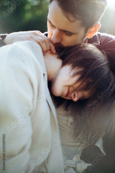 Obraz Loving hipster couple walking in the field, kissing and holding hands, hugging, lying in the grass in the spring at sunset. Photo with lens flare