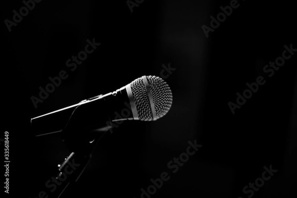 Fototapeta The microphone for the stage stands on a stand on a black background. Black and whire photography.