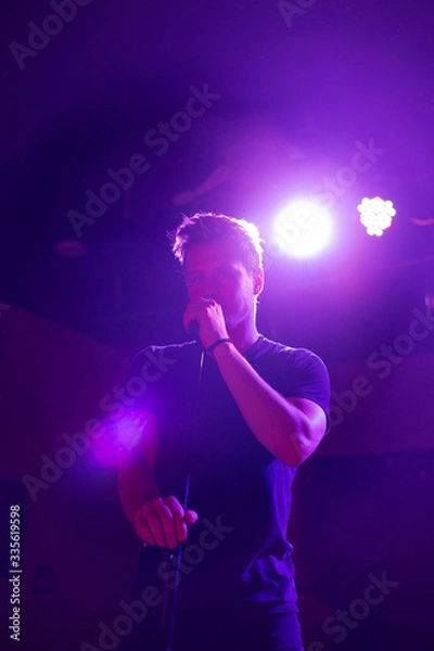 Fototapeta Young handsome guy emotionally sings and speaks into the microphone