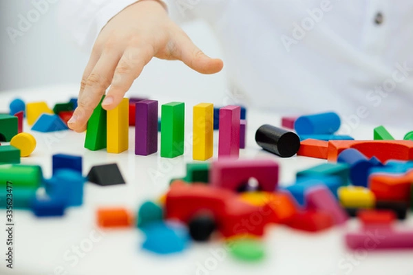 Fototapeta Building items in a single row. Concept of diagnostics of children's autism. A child plays with a colored wooden construction tool.
