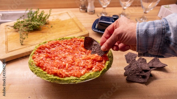 Fototapeta Casual middle aged man dipping into Mexican salsa dip while holding nacho tortillia chips