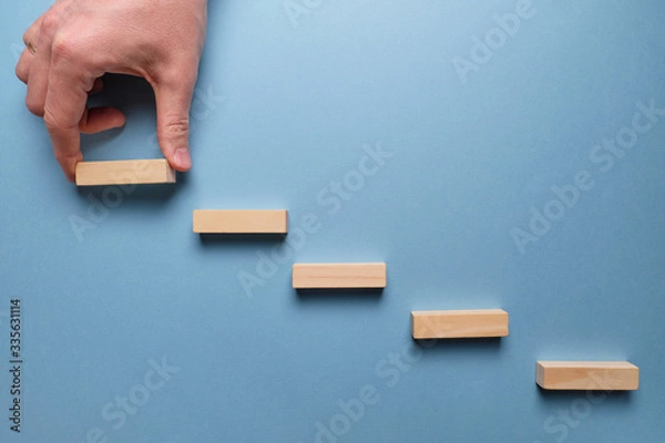 Fototapeta Concept of business development stages. Hand holds wooden blocks on a blue background.