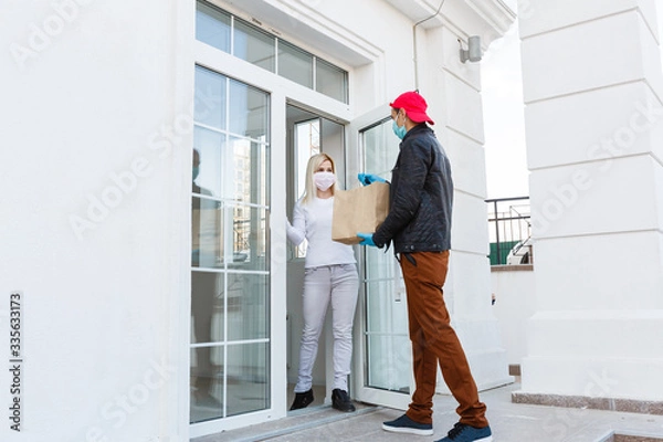 Fototapeta delivery man in protective mask and medical gloves holding a paper box. Delivery service under quarantine, disease outbreak, coronavirus covid-19 pandemic conditions.