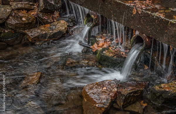Fototapeta Overflow from an autumn rain drains from pipes next to a stream
