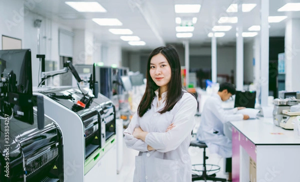 Fototapeta young smiling scientist in white lab coat standing with automation blood analyzer at medical laboratory