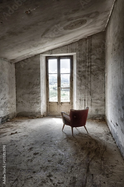 Fototapeta Butaca a contraluz en habitación sucia y abandonada iluminada por una ventana.