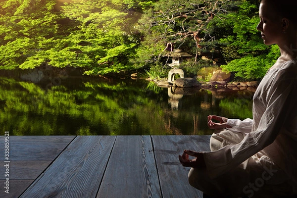 Fototapeta Beautiful young woman in white robe sits in meditation on the background of the zen garden..Meditation is the best way to solve the most complex problems.