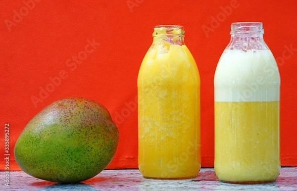Fototapeta Glass bottles filled with colorful fresh homemade mango smoothies on an orange background
