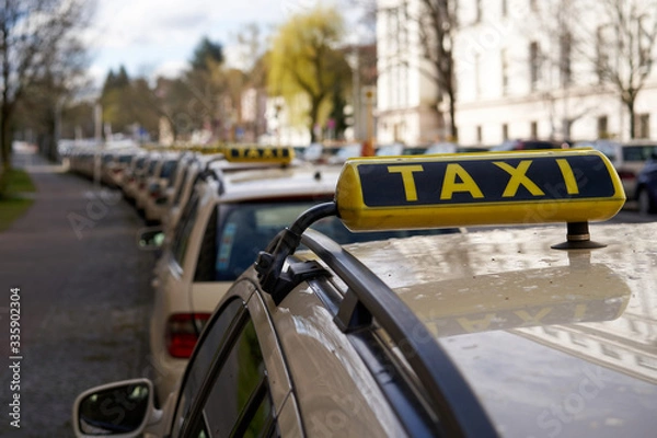 Fototapeta Berlin Germany, Line of yellow taxi cabs parking in a street in inner city of berlin. no passengers because of missing tourists, closup taxi sign