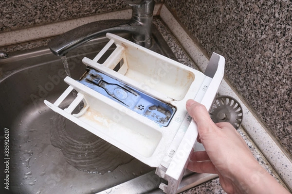 Fototapeta A person cleaning dirty moldy washing machine detergent and fabric conditioner dispenser drawer compartment. Mold, rust and limescale in washing machine tray. Home appliances periodic maintenance