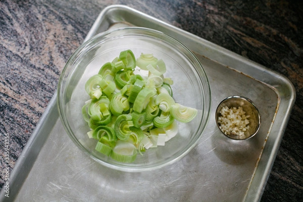 Fototapeta Freshly cut leeks in a glass bowl on marble surface
