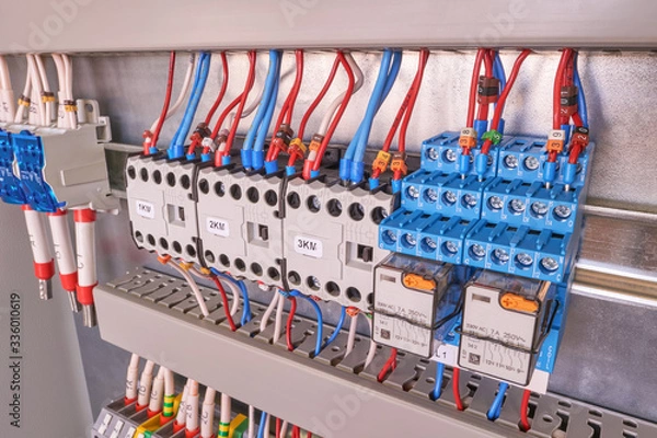Fototapeta Two intermediate relays, three contactors or magnetic starters, a cross-module and terminals in the electrical Cabinet. Wires and cables are connected to electrical equipment. Assembly manufacturing.