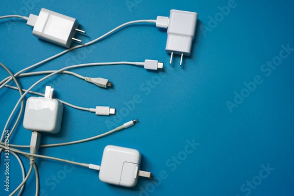 Fototapeta Top view or flat lay of White mobile power charger and USB in multiple types laid disorderly and mess on blue pvc sheet texture background , energy management concept ,with copy space