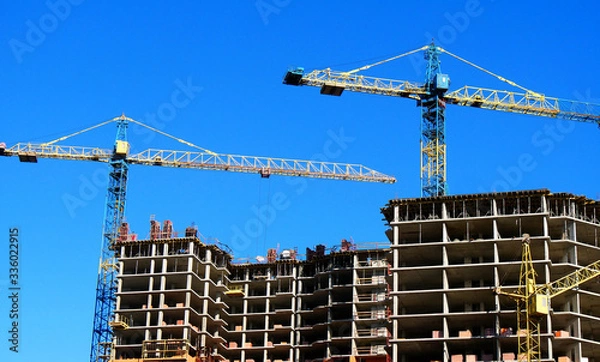 Fototapeta Concrete building under construction. Construction site. Two tower cranes near building.