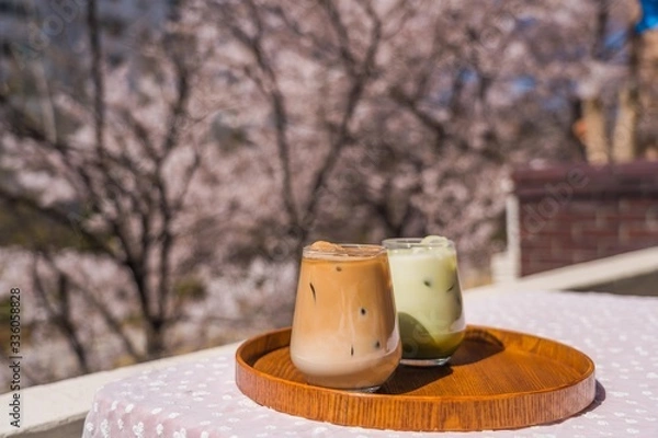 Obraz Enjoying spring in South Korea with a glass of Caffè Latte and Green Tea Latte on a wooden tray with pink cherry blossom sakura tree background.