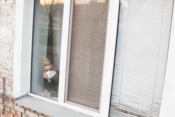Obraz Upset young man sitting on his birthday and looking out the window. The concept of loneliness in quarantine during the pandemic of the coronavirus COVID-19.