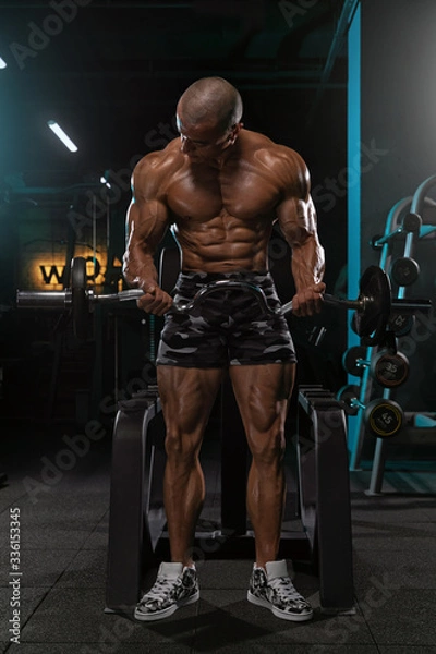 Fototapeta Man doing biceps exercise while standing with barbell.