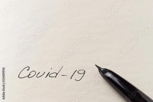 Fototapeta Covid-19 coronavirus inscription on a blank empty sheet of paper in a notebook. Nearby lies a pen. A lot of space for inscriptions and copyspace. Blank for inscriptions. Template for article or cover.