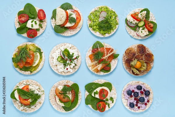 Fototapeta set of rice cakes on light blue background. healfy food rice cake sandwich isolated on light blue background. Rice cakes with Basil, tomatoes, avacado, cheese and red trout or salmon fish, mozerella