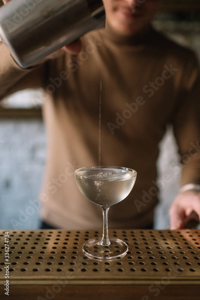 Obraz Bartender pouring a cocktail from a mixing pitcher into a cooled glass. Smooth image with shallow depth of field.